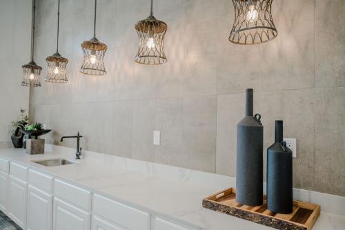 Apartments in Bluffton Modern kitchen with white cabinets, marble countertops, and a single black faucet. Five pendant lights hang above the counter. Two black decorative bottles are placed on a wooden tray.