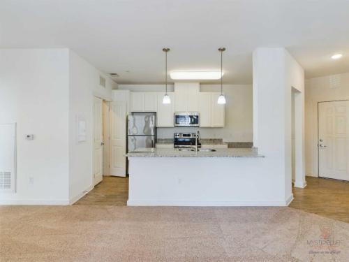 Apartments in Bluffton Modern kitchen with white cabinets, stainless steel appliances, granite countertops, and breakfast bar, viewed from a living area with carpeted flooring. Dual pendant lights hang above the bar.