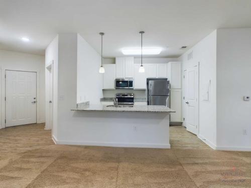 Apartments in Bluffton Modern kitchen with white cabinets, stainless steel appliances, granite countertops, and pendant lights, viewed from a carpeted living area. Doorways lead to additional rooms on the left and right.