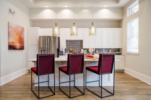 Apartments in Bluffton Modern kitchen with white cabinets, stainless steel appliances, pendant lights, and a central island. Three red cushioned bar stools are positioned along the island countertop.