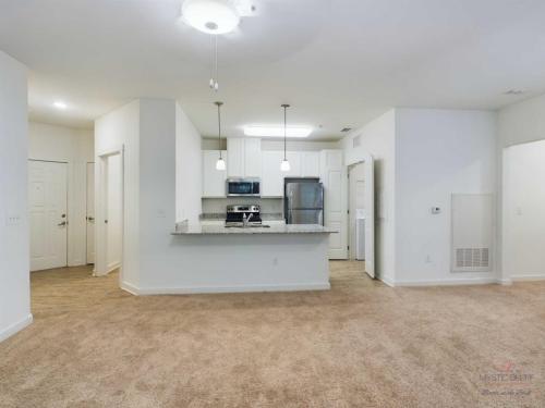 Apartments in Bluffton Modern, unfurnished kitchen and living area with white walls, carpet flooring, and recessed lighting. Kitchen features white cabinets, stainless steel appliances, and a breakfast bar with pendant lights.