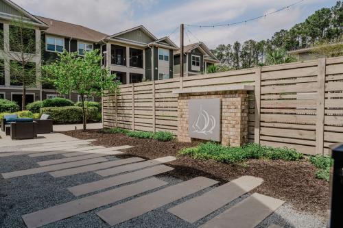 Apartments in Bluffton Outdoor area with modern apartment buildings in the background. The foreground features a paved pathway, a wooden fence with a decorative mural, and small greenery.