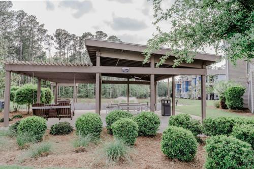 Apartments in Bluffton Outdoor pavilion with wooden benches and picnic tables, surrounded by trimmed bushes and trees, located near a residential area.