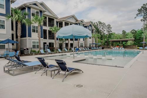 Apartments in Bluffton Outdoor swimming pool area at an apartment complex with lounge chairs, umbrellas, and surrounding multi-story buildings.