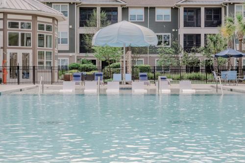 Apartments in Bluffton Outdoor swimming pool with in-water lounge chairs and umbrellas, situated in front of an apartment building.
