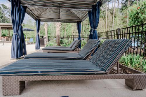 Apartments in Bluffton Poolside cabana with four striped lounge chairs under a canopy, enclosed by a black metal fence, with greenery and trees in the background.