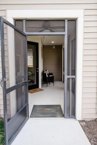 Apartments in Bluffton Screen door open to a small porch with a black chair and cushion, a welcome mat, facing the beige siding of a house.