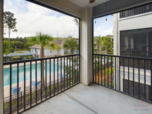 Apartments in Bluffton View from a balcony showing a swimming pool area with loungers, surrounded by buildings and palm trees in a residential complex.