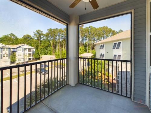 Apartments in Bluffton View from a balcony with metal railings overlooking a parking lot and residential buildings surrounded by trees. The balcony has a ceiling fan.